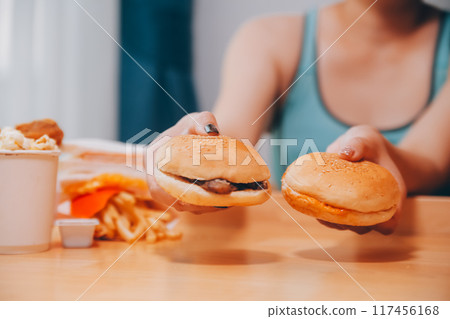 Binge eating disorder concept with woman eating fast food burger, fired chicken , donuts and desserts Binge eating disorder concept with woman eating fast food burger, fired chicken , donuts and desserts 117456168