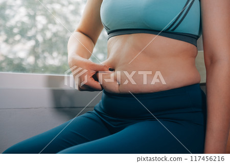 fat woman, fat belly, chubby, obese woman hand holding excessive belly fat with measure tape, woman diet lifestyle concept 117456216