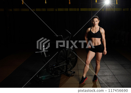 Slim and fit female model with perfect abdomen muscles in dark gym Slim and fit female model with perfect abdomen muscles in dark gym 117456690