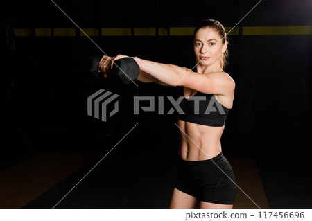 Fit young woman holding a dumbell while working out at a gym Fit young woman holding a dumbell while working out at a gym 117456696