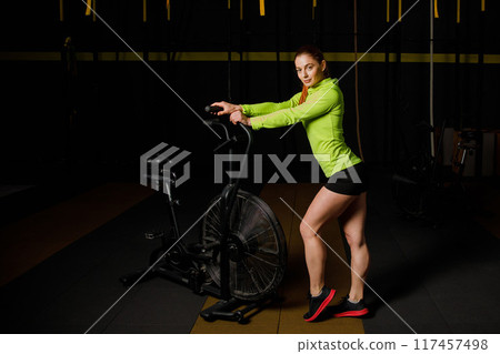 A young muscular woman is doing hard bike crossfit training in the gym. A young muscular woman is doing hard bike crossfit training in the gym. 117457498