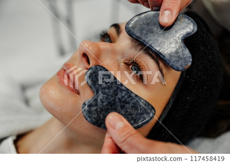 Relaxing facial treatment with gua sha stones at a spa during the day in a calm setting 117458419