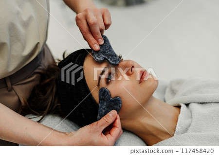 Woman enjoying relaxing facial treatment with gua sha tool in spa on a calm afternoon Woman enjoying relaxing facial treatment with gua sha tool in spa on a calm afternoon 117458420