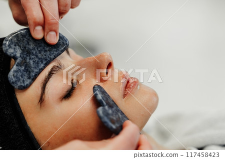 Relaxing facial treatment using gua sha tools at spa during afternoon Relaxing facial treatment using gua sha tools at spa during afternoon 117458423