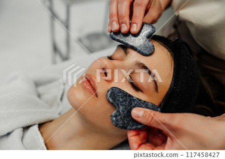 Woman receiving facial treatment with smooth stones in a spa setting during daytime Woman receiving facial treatment with smooth stones in a spa setting during daytime 117458427