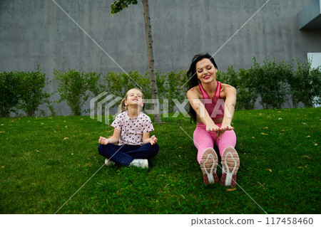 Mother and daughter stretching together on a grassy lawn during a sunny afternoon Mother and daughter stretching together on a grassy lawn during a sunny afternoon 117458460