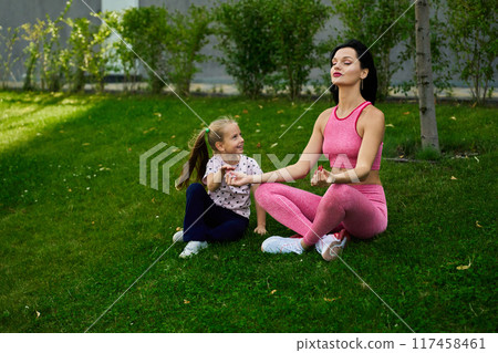 Mother and daughter practicing meditation on green grass in a peaceful outdoor setting 117458461