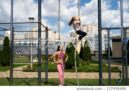 Mother and daughter enjoy climbing ropes at a playground on a sunny day in a city park 117458486