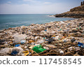 Vast accumulation of plastic waste along rocky shoreline under clear blue sky 117458545