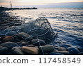 Empty fishing net resting on pebbled shoreline with calm waters at dusk 117458549
