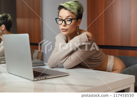 A beautiful girl with short hair in her underwear is sitting sexy in a room at a laptop, working and chatting online 117458550