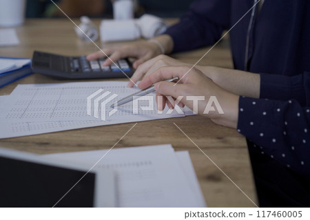 Accountants or auditors reviewing financial documents while sitting at the wooden desk in office. Professionals analyzing paper reports and using calculators, close up. Audit and taxes concept 117460005