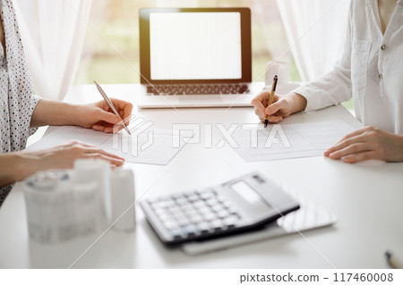 Two accountants using a laptop computer for counting taxes at white desk in office. Teamwork in business audit and finance Two accountants using a laptop computer for counting taxes at white desk in office. Teamwork in business audit and finance 117460008