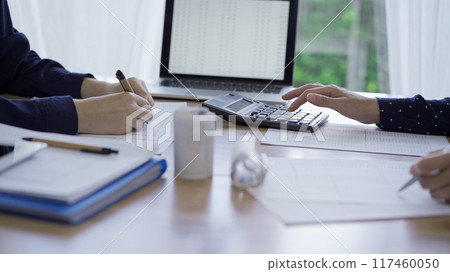 Accountants or auditors reviewing financial documents while sitting opposite one another at the wooden desk in office. Audit and taxes 117460050