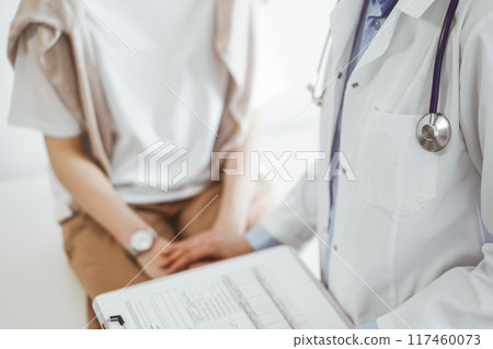 Doctor and patient in clinic. Friendly physician examining a young woman with a one hand while keeping a clipboard with medical records in another. Medicine concept Doctor and patient in clinic. Friendly physician examining a young woman with a one hand while keeping a clipboard with medical records in another. Medicine concept 117460073
