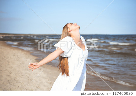 Happy smiling beautiful woman is on the ocean beach in a white summer dress, open arms Happy smiling beautiful woman is on the ocean beach in a white summer dress, open arms 117460080