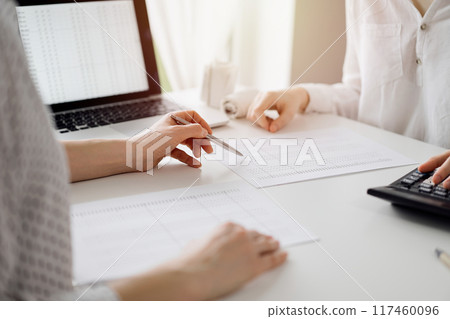 Accountant using a calculator and laptop computer for counting taxes with a client or a colleague at white desk in office. Teamwork in business audit and finance 117460096