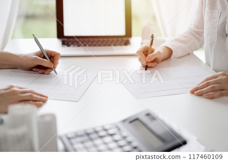 Two accountants using a laptop computer for counting taxes at white desk in office. Teamwork in business audit and finance Two accountants using a laptop computer for counting taxes at white desk in office. Teamwork in business audit and finance 117460109