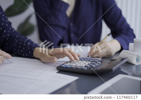 Female accountants or auditors reviewing financial data in office. Professionals analyzing paper reports and using calculator, close up. Audit and taxes concept 117460117