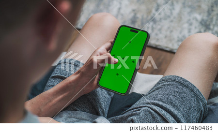 Caucasian teenager scrolls mobile phone with chroma key mockup 117460483