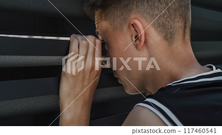 Caucasian teenager peeking through gap between the iron fence Caucasian teenager peeking through gap between the iron fence 117460541