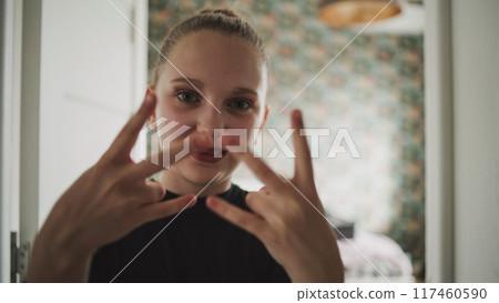 Adorable and happy young girl makes funny hand gestures on camera Adorable and happy young girl makes funny hand gestures on camera 117460590