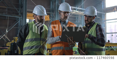 Three industry technicians talk about production, use laptop in factory 117460598