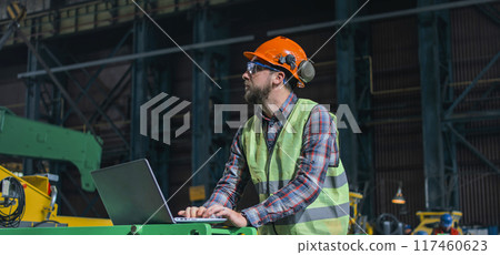 Male worker manages the work of industrial equipment and uses laptop Male worker manages the work of industrial equipment and uses laptop 117460623