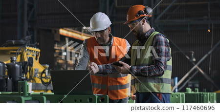 Two heavy industry engineers work using laptop and mobile phone at factory Two heavy industry engineers work using laptop and mobile phone at factory 117460696