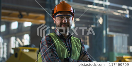 Male engineer smiles and looks at camera standing at manufacturing factory Male engineer smiles and looks at camera standing at manufacturing factory 117460709