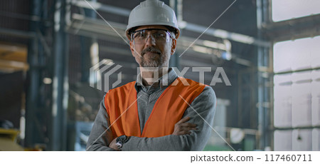 Mature heavy industry engineer in safety uniform and hard hat looks at camera 117460711