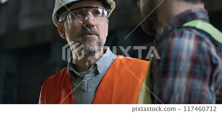 Close up of mature engineer talking with colleague standing at factory 117460712