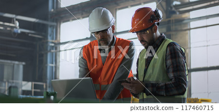 Two industry technicians stand in warehouse, work on laptop and mobile phone Two industry technicians stand in warehouse, work on laptop and mobile phone 117460715
