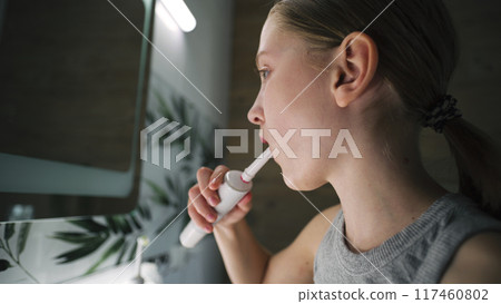 Young girl looks at mirror in bathroom, brushes her teeth 117460802
