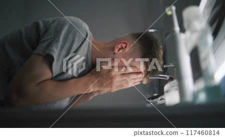 Boy washes face with cold water and wipes hands using towel 117460814