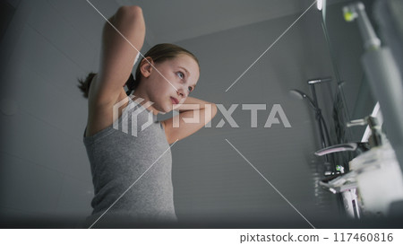 Young girl looks at the mirror in bathroom and combs her hair 117460816