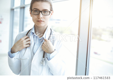 Beautiful woman doctor with stethoscope smiling charmingly and ready to help patients in sunny hospital. Medicine concept Beautiful woman doctor with stethoscope smiling charmingly and ready to help patients in sunny hospital. Medicine concept 117461583
