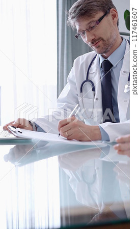 Doctor consulting patient. Male physician is pointing into medical records on a clipboard while talking with a woman in a clinic, close up. Medicine concept 117461607