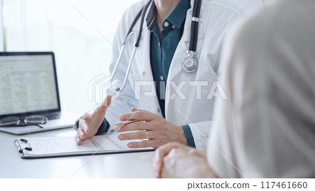 Doctor and a patient. The physician, wearing a white medical coat over a green shirt, is gesturing with his hands during a consultation in the clinic. Medicine 117461660