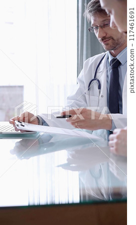 Doctor consulting patient. Male physician is pointing into medical records on a clipboard while talking with a woman in a clinic, close up. Medicine concept Doctor consulting patient. Male physician is pointing into medical records on a clipboard while talking with a woman in a clinic, close up. Medicine concept 117461691