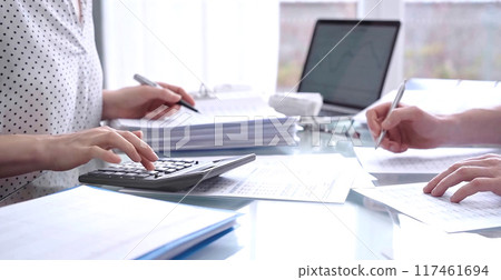 Business colleagues accountants or auditors reviewing financial data in office. Two professionals analyzing paper reports and using calculators. Audit and taxes 117461694