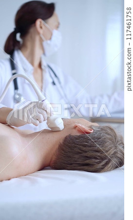 Doctor woman with white medical gloves performing neck ultrasound exam on male patient. Thyroid gland examination. Medicine concept 117461758