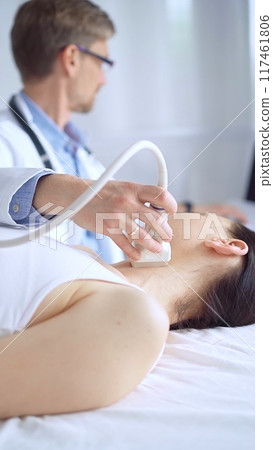 Doctor man using ultrasound equipment on the neck of a patient woman, lying for examination. Medicine concept 117461806