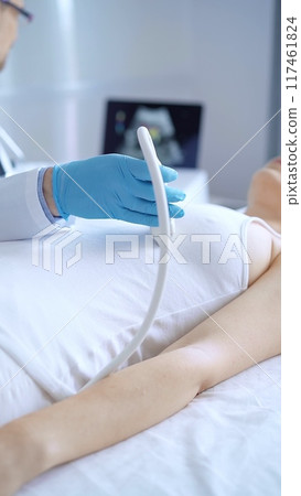 Doctor man wearing blue protective gloves is using ultrasound equipment on the breast of a female patient. Mammary gland health. Medicine concept 117461824