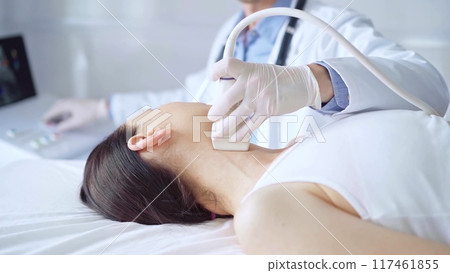 Doctor man is using ultrasound equipment on neck of female patient lying down for a medical examination. Medicine and science 117461855