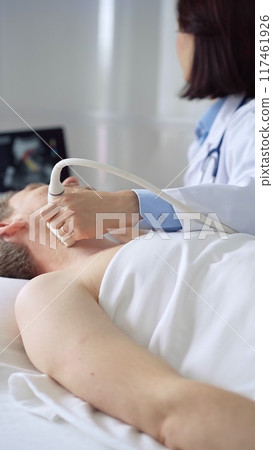 Doctor performing neck ultrasound exam on male patient 117461926