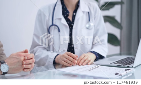 Doctor and patient are talking in clinic. Female physician is sitting and discussing test results with a senior man. Medicine and science 117461939