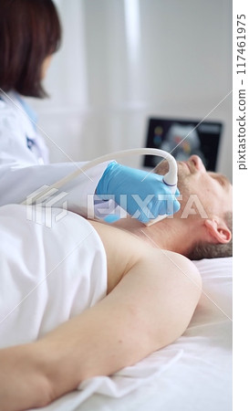 Doctor woman with blue medical gloves performing neck ultrasound exam on male patient Doctor woman with blue medical gloves performing neck ultrasound exam on male patient 117461975