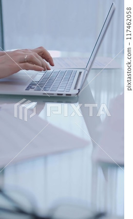 Business woman is working with laptop computer while sitting at the glass table in home office, closeup of hands 117462058