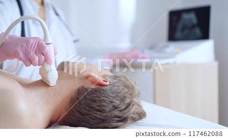 Doctor woman with pink medical gloves performing neck ultrasound exam on male patient. Thyroid gland examination. Medicine service concept Doctor woman with pink medical gloves performing neck ultrasound exam on male patient. Thyroid gland examination. Medicine service concept 117462088